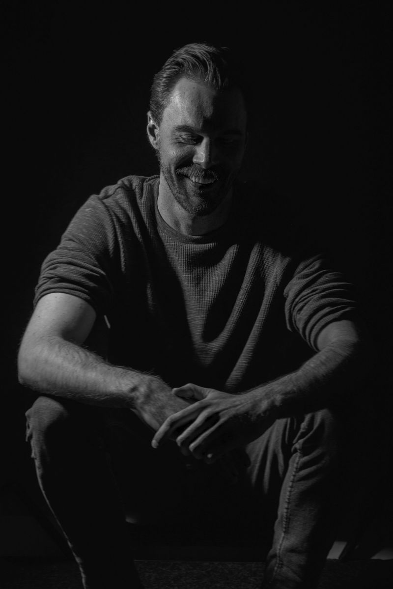Pete Zbrojkiewicz in black and white, one hand resting against his head, looking down in thought.